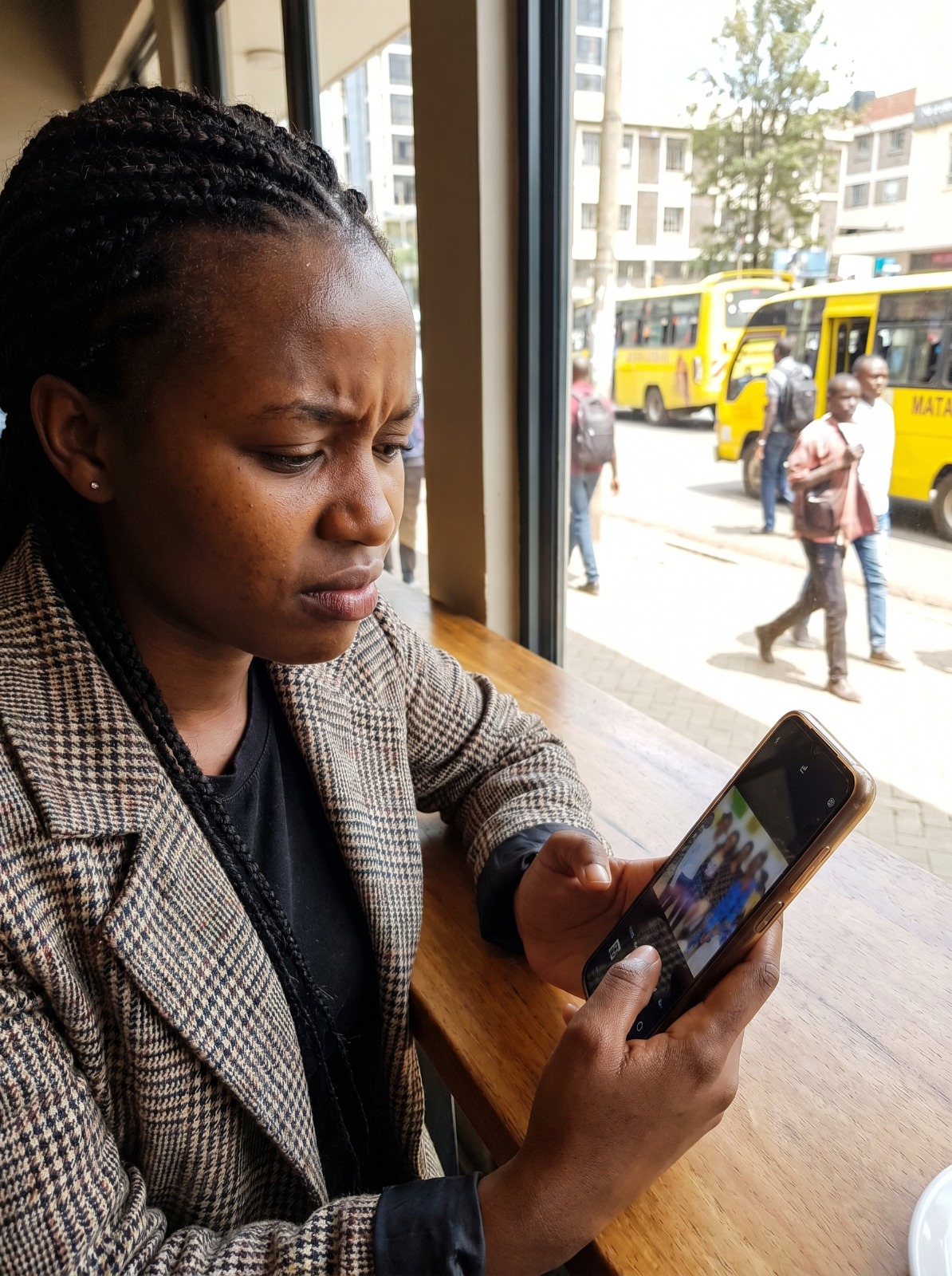 A young Nairobi woman staring at her phone in soft daylight, slightly frowning at a group photo on her screen