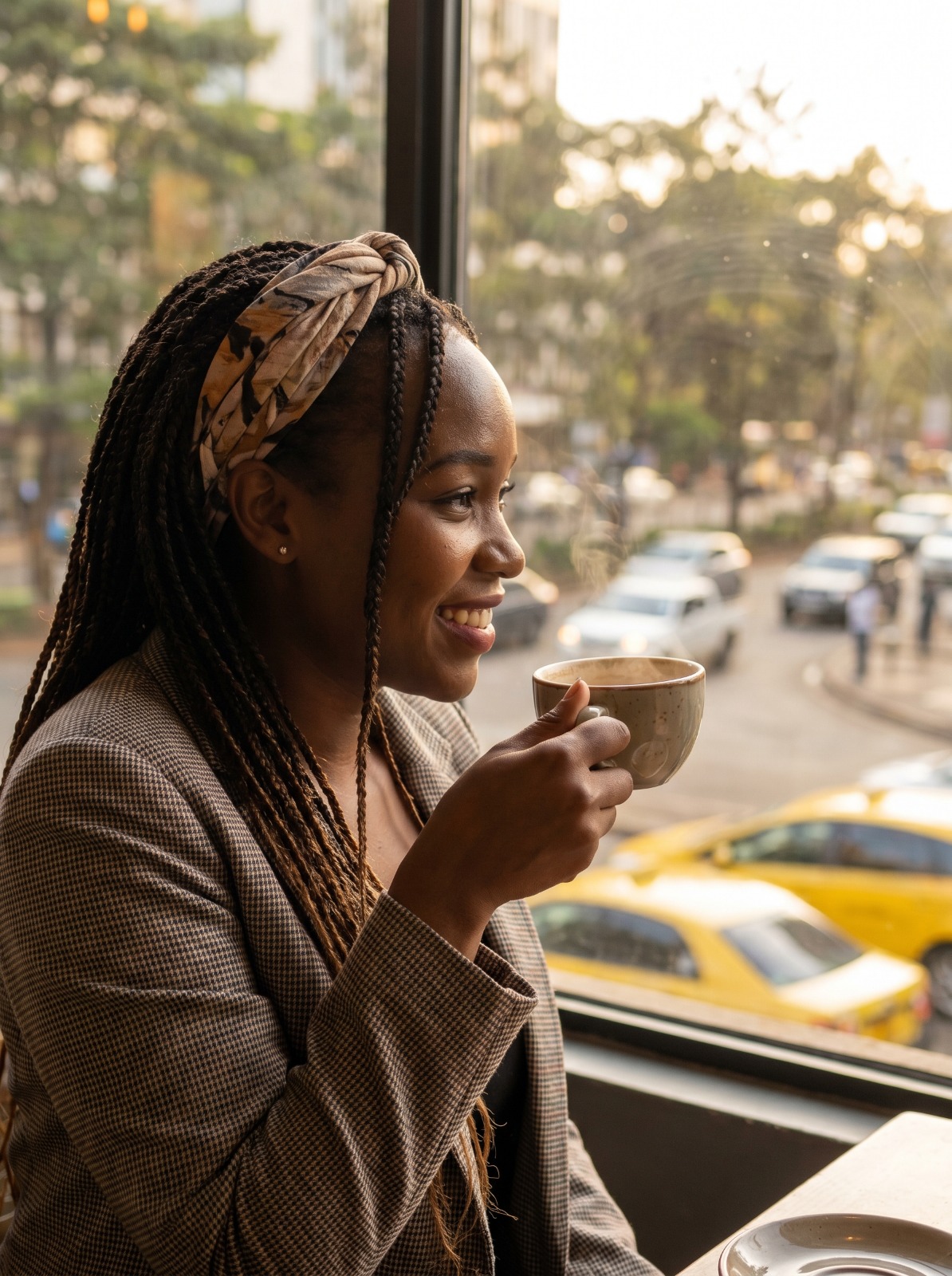 A stylish Nairobi woman holding a cup of chai by a window, soft golden light reflecting on her smile