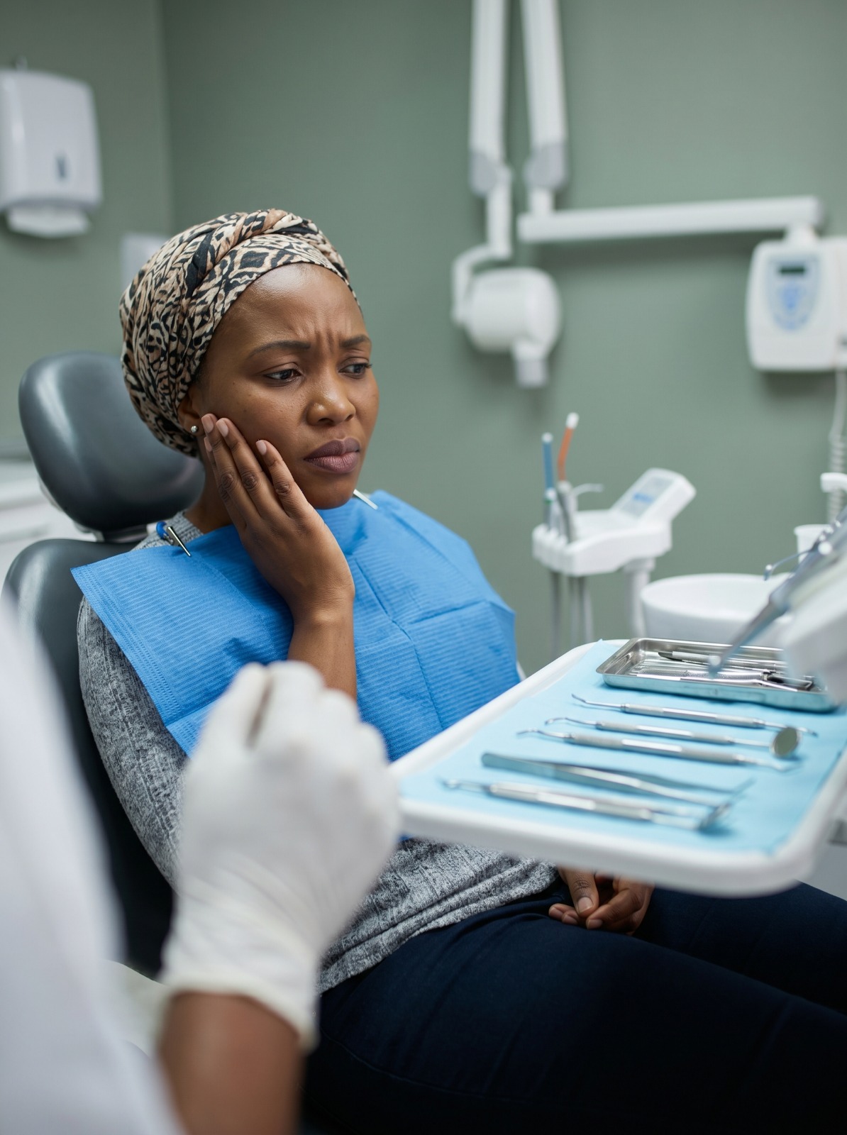 Woman holding her cheek with slight discomfort while looking at dental tools, symbolizing fear of sensitivity